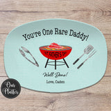 One Rare Daddy grilling platter with blue background and red grill with 1st Father's Day in the center with a rare steak on the grates. BBQ tongs, spatula, fork on the left and right of the grill. Well Done with Love and names at the bottom