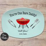 One Rare Daddy grilling platter with blue background and red grill with 1st Father&#39;s Day in the center with a rare steak on the grates. BBQ tongs, spatula, fork on the left and right of the grill. Well Done with Love and names at the bottom