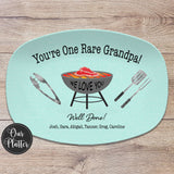 One Rare Grandpa grilling platter with blue background and gray grill in the center with a rare steak on the grates. BBQ tools tongs, spatula and fork on the left and right of the grill. Well Done with Love and the names at the bottom